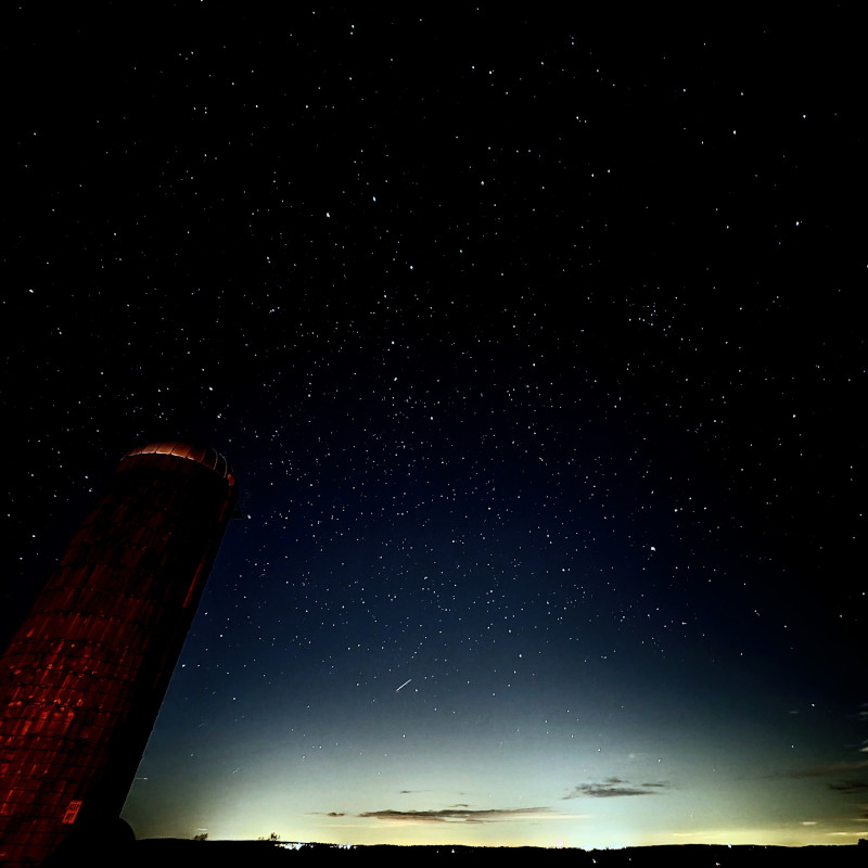 A clear, starry night sky above a silo on a hilltop farm